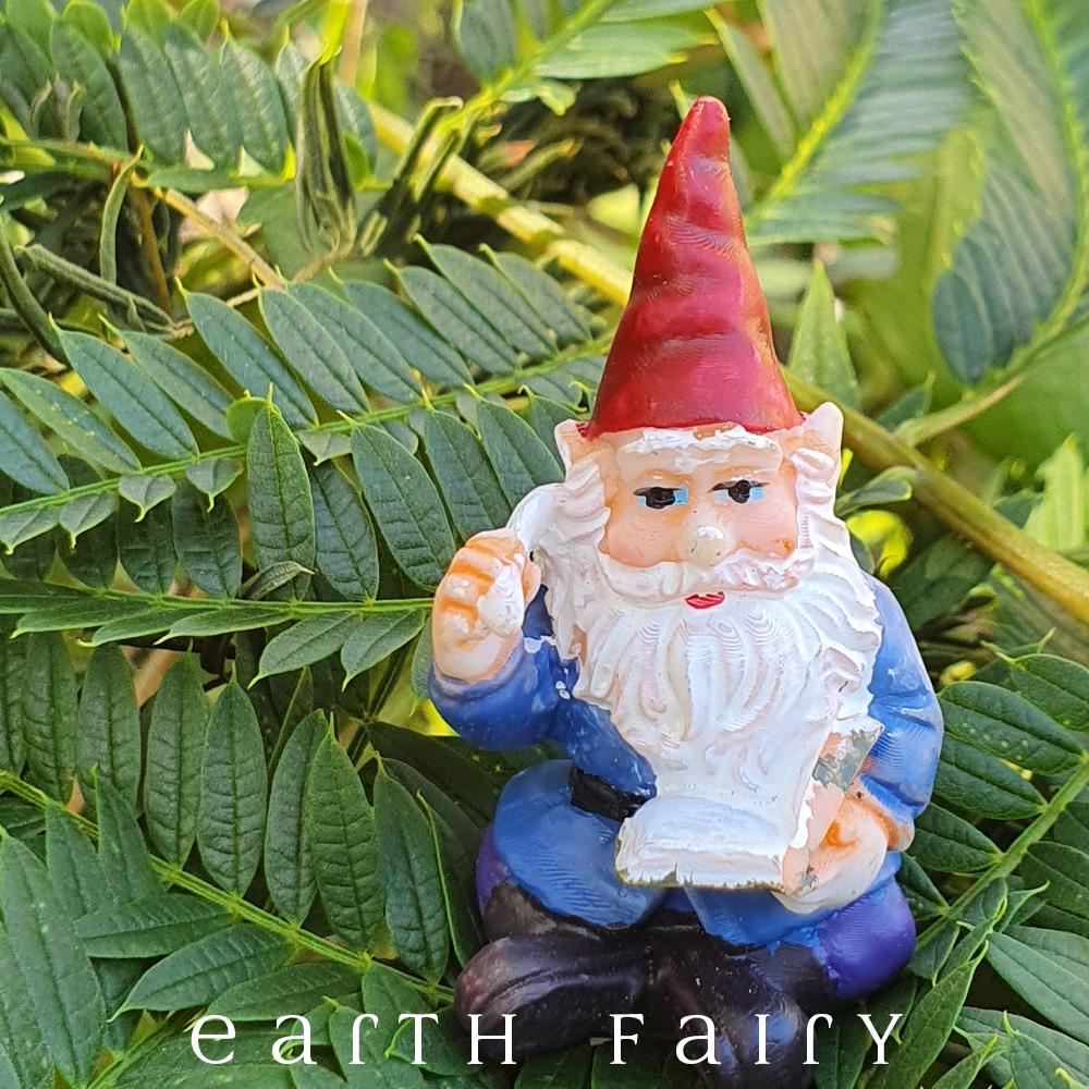 Miniature polyresin gnome figurine, dressed in boots, purple pants, blue coat and red pointy hat, sitting with a book