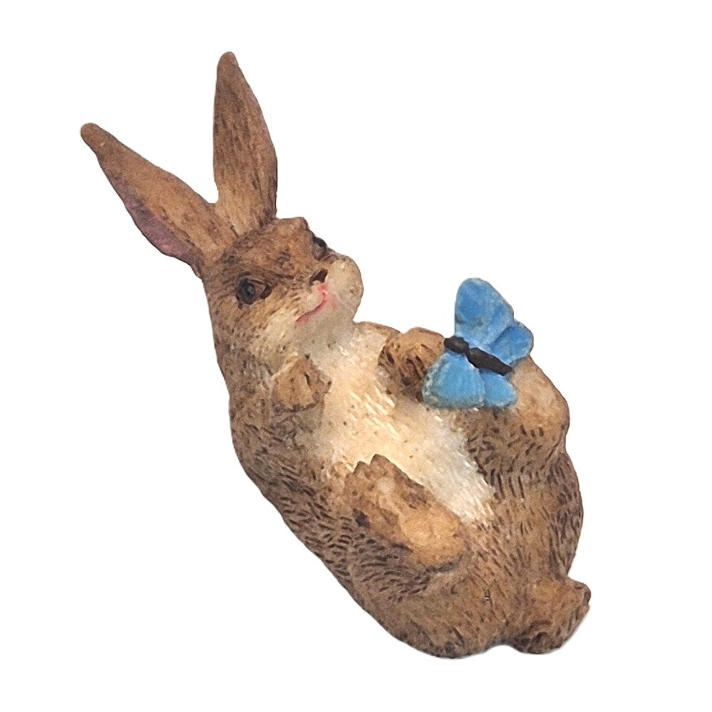 Overhead view of bunny rabbit figurine on his back playing with blue butterfly - Earth Fairy