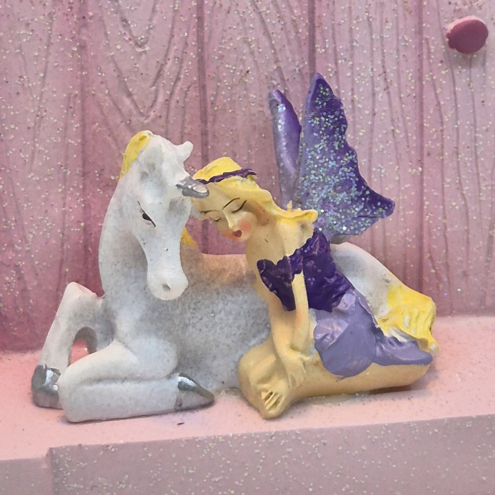 Close up of purple fairy and white unicorn figurines on pink fairy door step