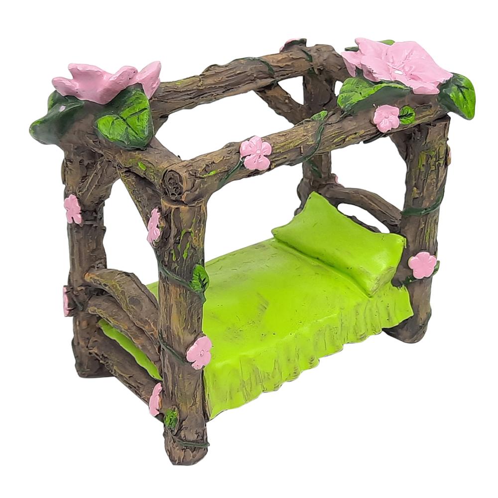 Miniature Fairy Bed with Flower Canopy, a four poster style bed fashioned from wood effect branches, with pink flowering vine twisting around its supports and a green pillow and blanket on the bed