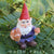 sitting miniature polyresin gnome, dressed in brown boots, blue pants, purple coat and red pointy hat, holding a pot of mushrooms