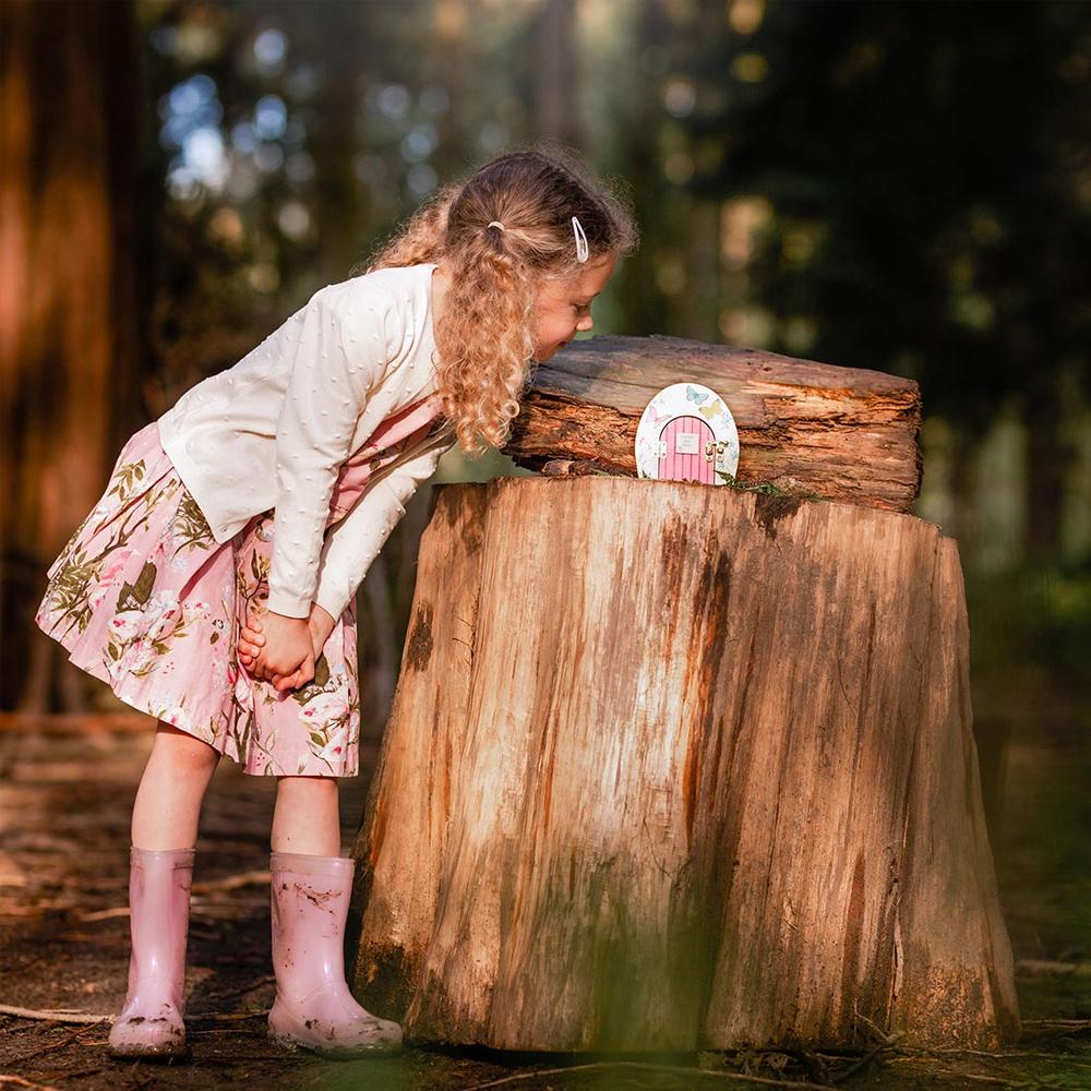 Truly Fairy Wooden Fairy Door, Fairy Themed Party Decoration, displayed sitting on a tree trunk with little girl observing