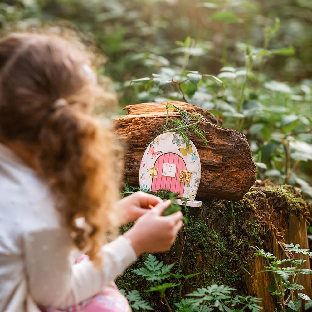 Truly Fairy Wooden Fairy Door, Fairy Themed Party Decoration, displayed in a garden setting, with little girl sitting nearby