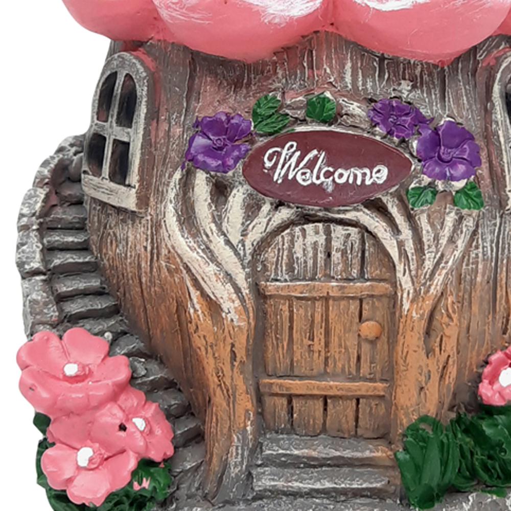 Close up view of the doorway of the Welcome Fairy Flower House, a miniature fairy house for the garden, with tree trunk style base and pink flower roof and winding staircase to the side displayed on a blank background